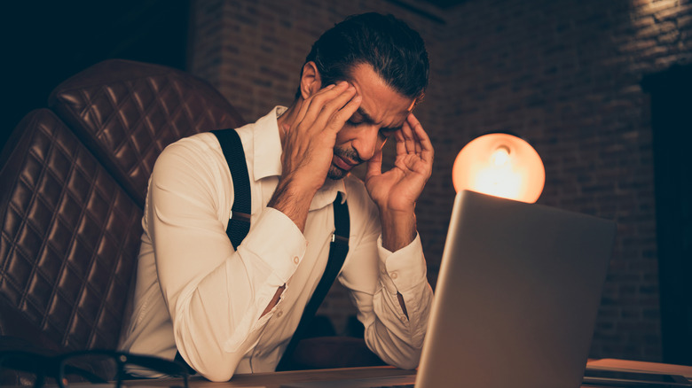 Wealthy man in stylish attire sitting in a decorated office with his face in his hands, signifying financial mistakes.