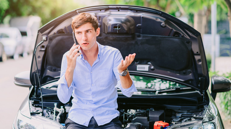 Man calling on cell phone while seated on car with open hood