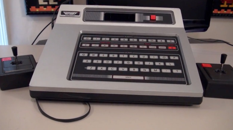 A Magnavox Odyssey 2 with two joysticks on a white desk