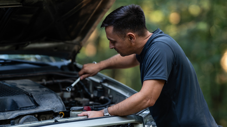 A middle-aged man uses a wrench to repair an engine problem on an SUV