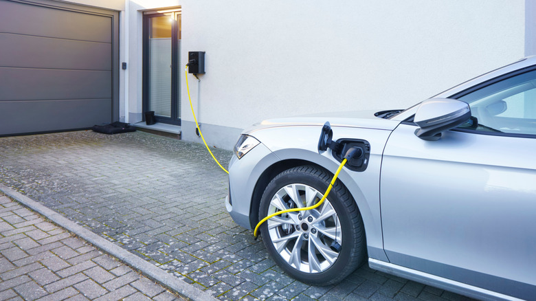 An EV parked in the driveway of a home charging from a wall box.