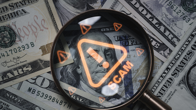 Magnifying glass focusing on scam warning symbol over dollar bills.
