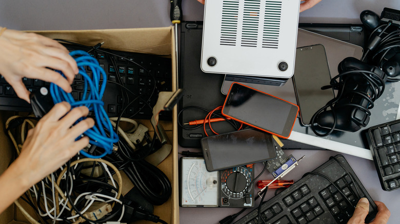 A person putting old computer parts, smartphone and cables into cardboard box for recycling.