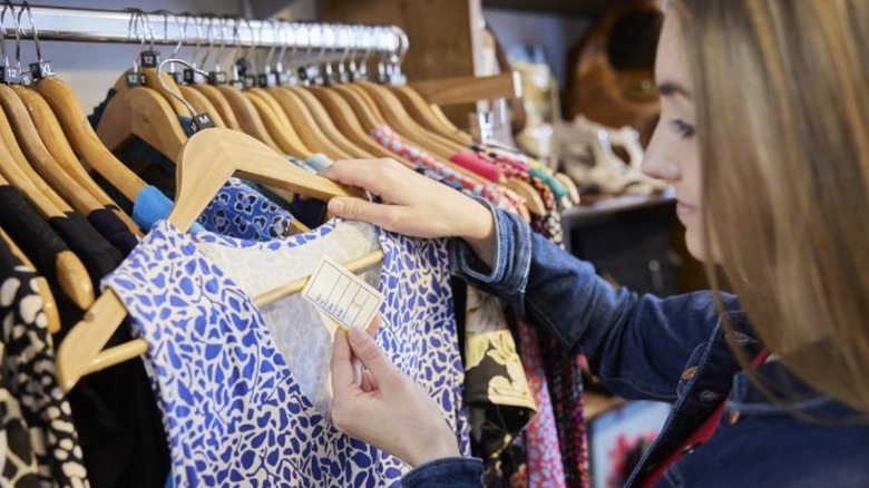 A woman looking at a price tag while shopping for dresses in a clothing store.