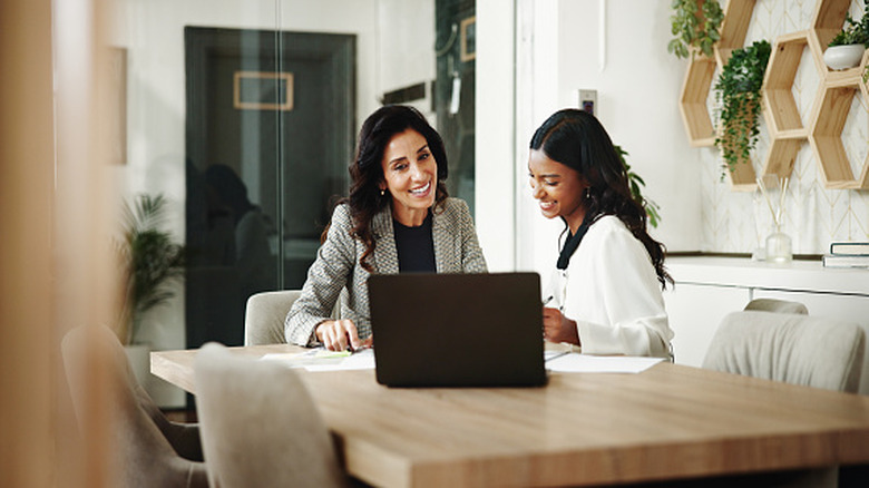 Two women at a desk looking at some documents and a laptop