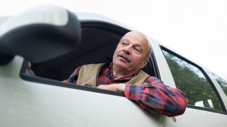 A frustrated older male driver looks out the window of a large white car