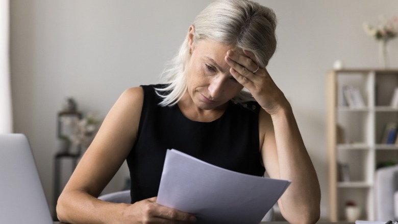 A worried middle-aged woman looking at financial documents.