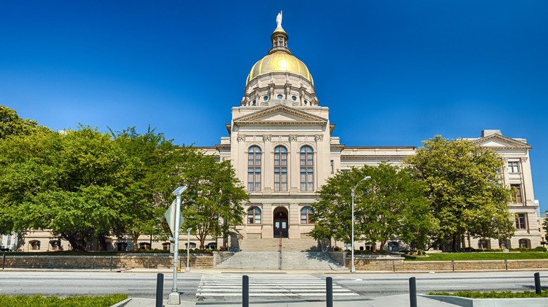 Front view of Georgia State Capitol building in Atlanta with a gold dome, framed by trees under a clear blue sky