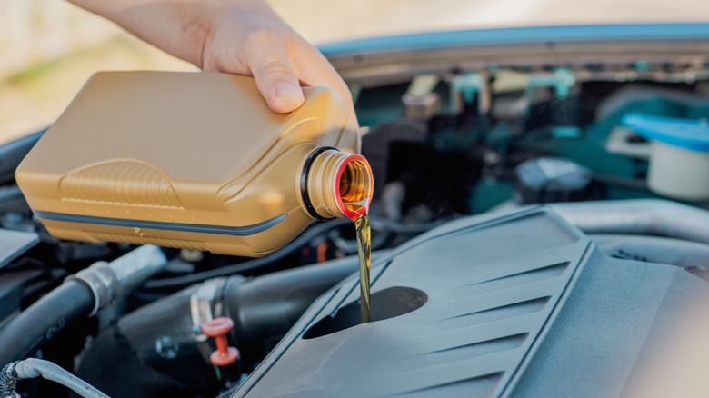 A person pours fresh motor oil from a plastic bottle into a car engine under an open hood