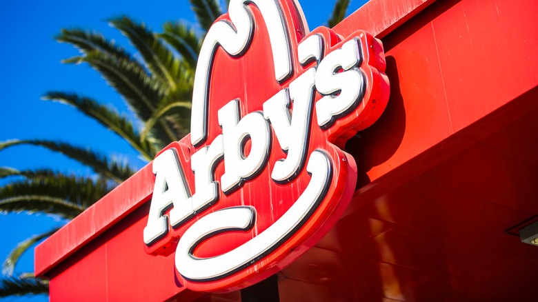 A close-up view of the iconic red Arby's logo sign against a bright blue sky.