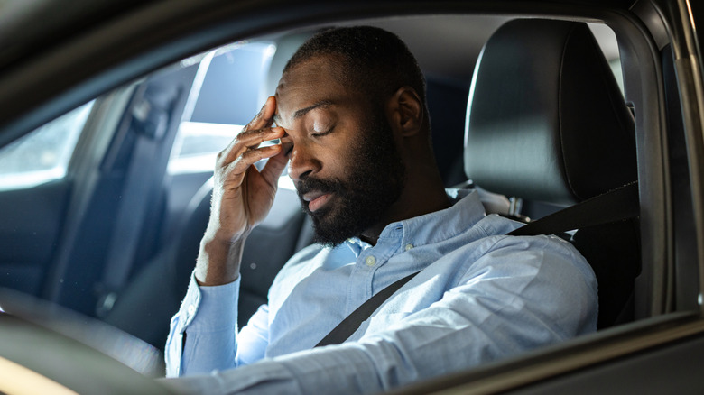 A man sits behind the wheel of a car looking frustrated