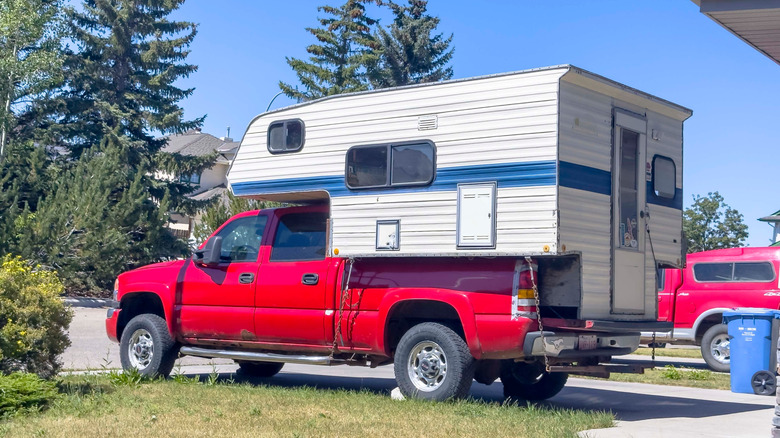 A red double cab pickup truck with an old camper in the bed.