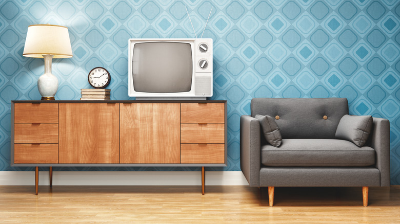 An old chair next to an entry table with a console TV, lamp, and clock on it.