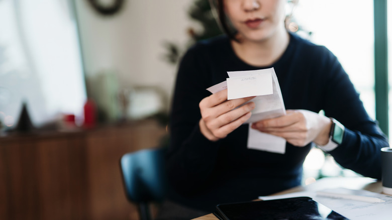 Woman at home, sitting at table, looks at receipts