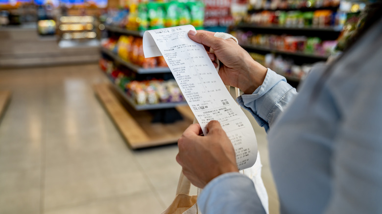 Pair of hands holding grocery receipt in grocery store