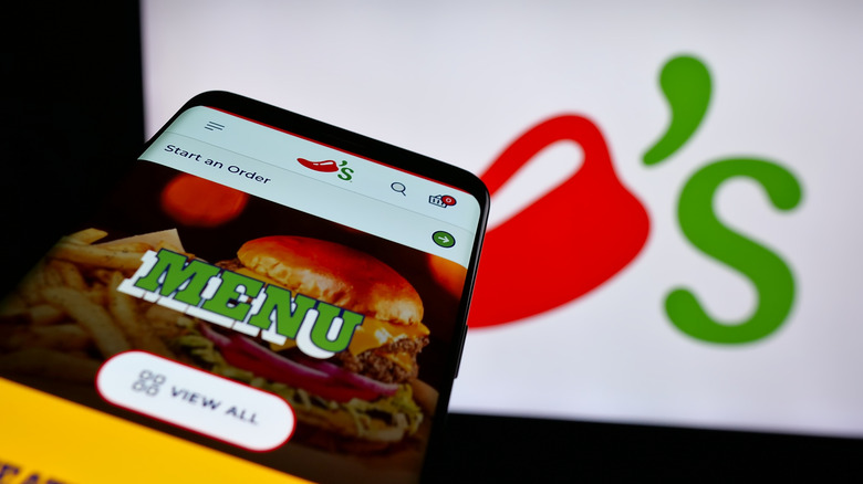 Close up of smartphone with Chili's app opened to Menu option with restaurant logo in the background