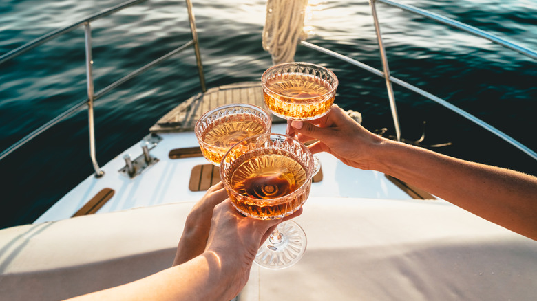 A close-up shot of friends clinking sparkling wine glasses at sunset on a yacht.