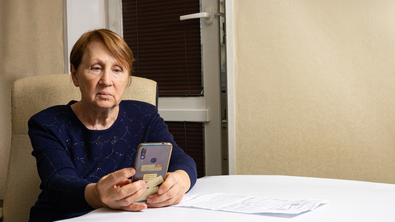 retiree looking at her cell phone with bill on table