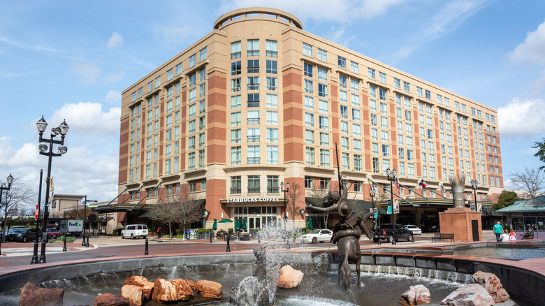 View of Sugar Land Town Square, with fountain, sculptures, building, city traffic and people.