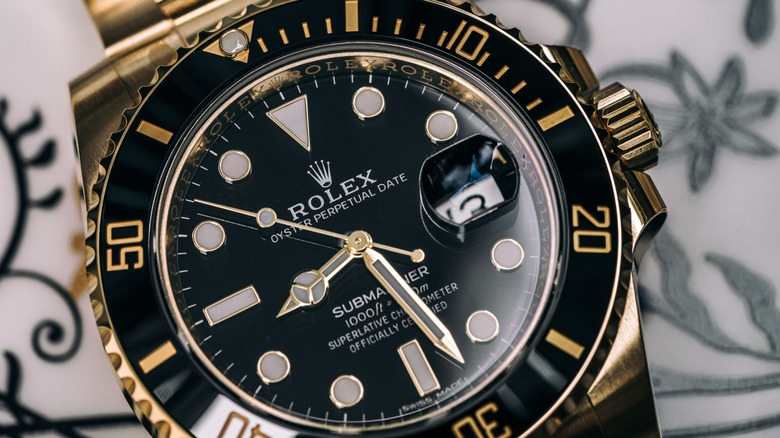Close-up of a two-tone gold and black Rolex Submariner with a black dial, gold hour markers, and a date window under a magnifying cyclops lens