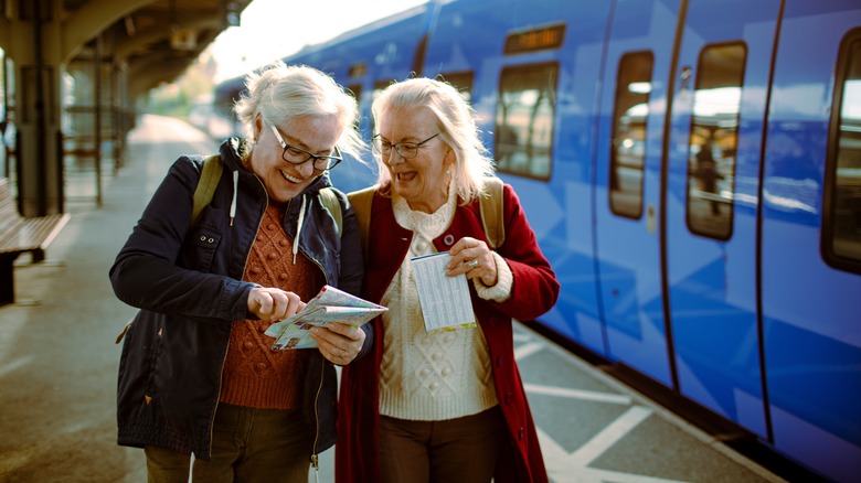Two senior women at train station with map