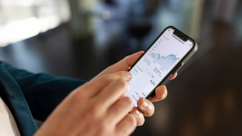 Hands holding smartphone with financial markets chart on screen