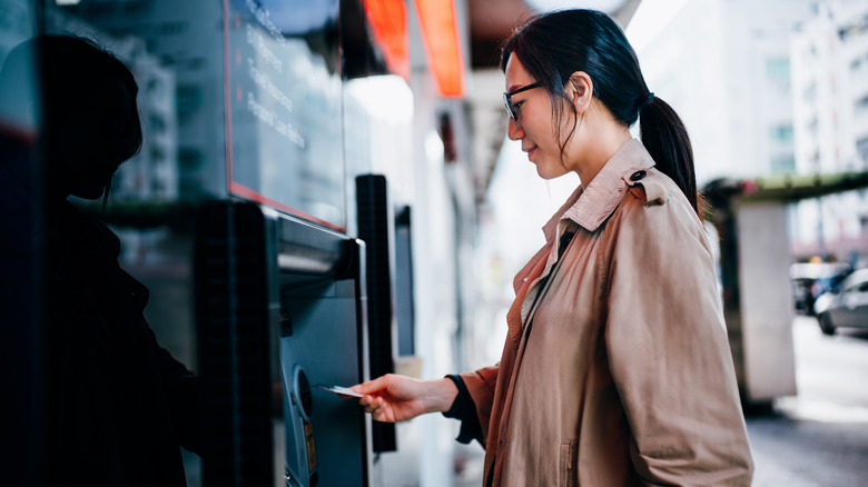 Young woman using card at outdoor ATM