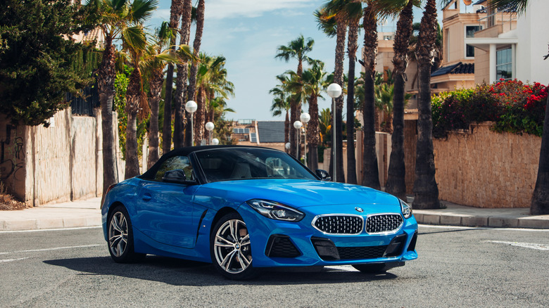 A blue BMW Z4 convertible driving down a palm tree-lined street in Spain