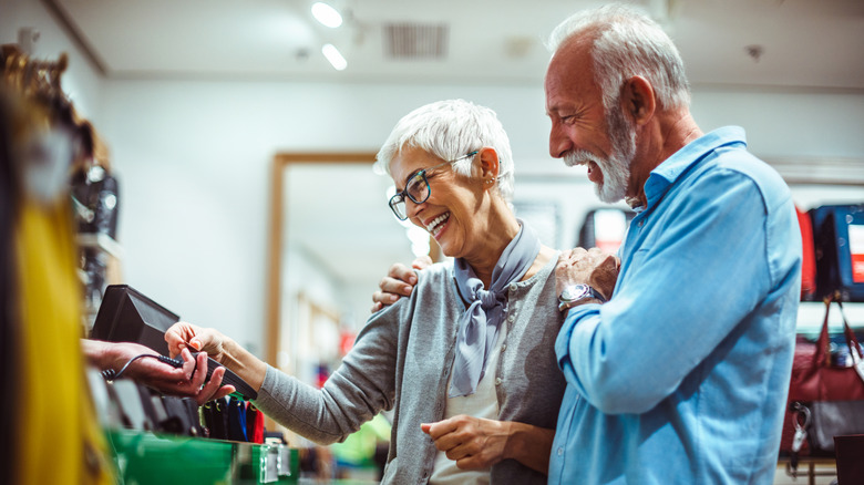 A happy retired couple using a credit card machine to buy something in a store.