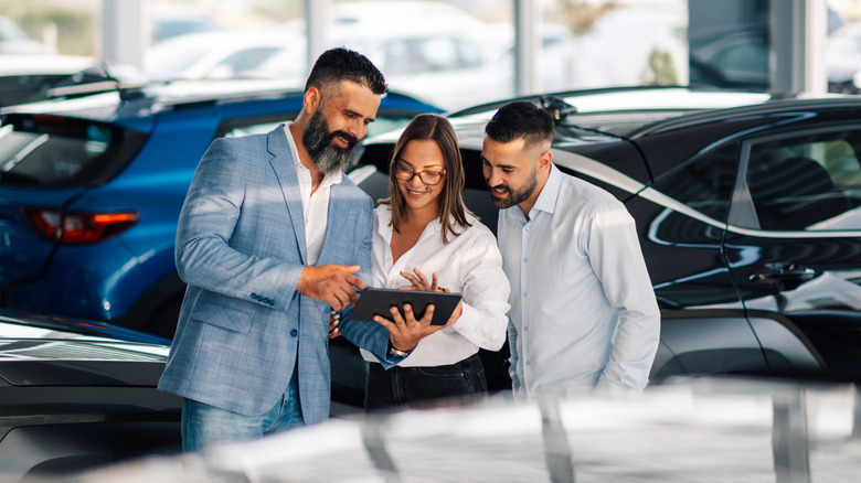 Prodavač automobila pokazuje mladom paru podatke na tabletu u prodajnom salonu