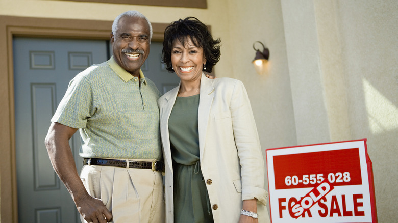 Boomer aged couple in front of a home and a sold sign