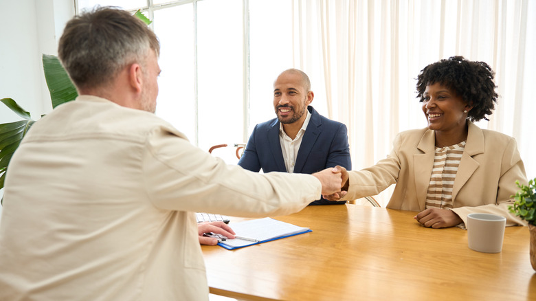 A pair of smiling young professionals shake hands with a banker approving their loan