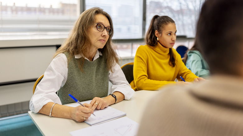 woman in classroom listening intently an taking notes