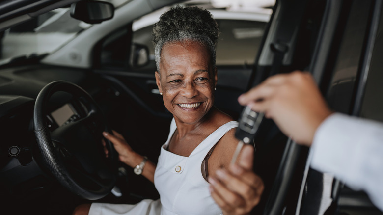 A smiling retired woman getting keys to her new car