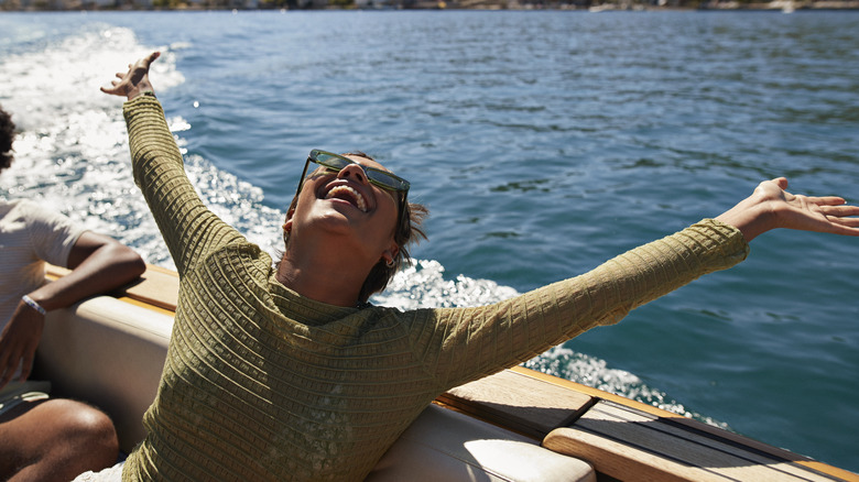 Happy young woman with arms raised in motorboat enjoying sunny day