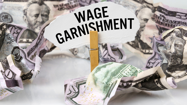 Wash clip holding up sign saying "Wage Garnishment" amongst crumpled dollar bills