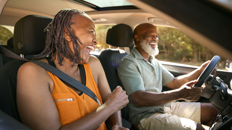 A smiling older couple riding in a car while the man drives