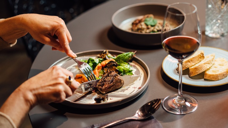 Plates of food being cut up by hands of diner
