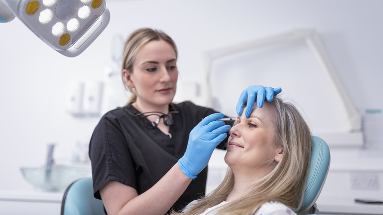 Cosmetic nurse injecting botox into patient in dental surgery