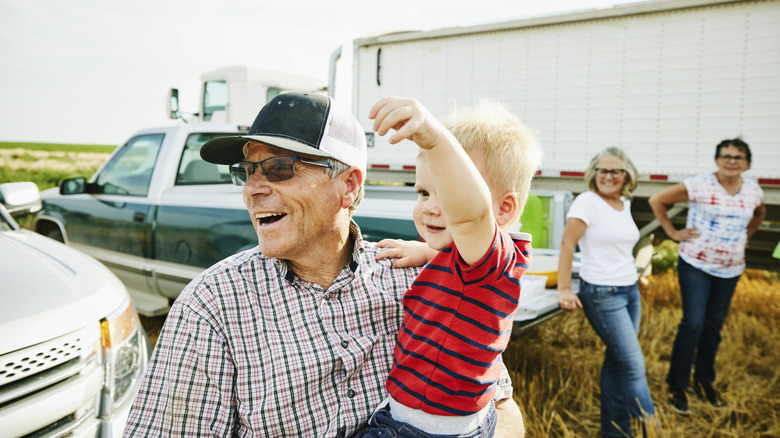 An elderly man holding a young child while two elderly women look on in the background