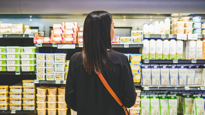 A young woman comparing the prices of butter and other dairy products