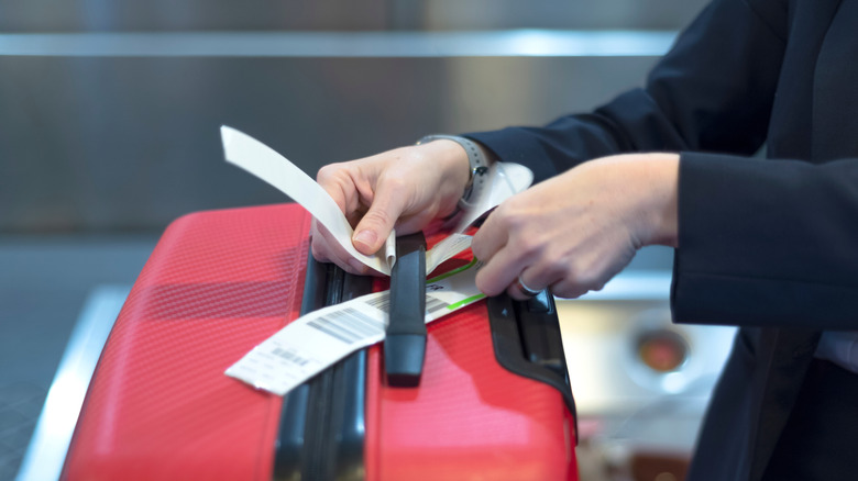 A check-in employee attaching a luggage tag to suitcase of passenger -