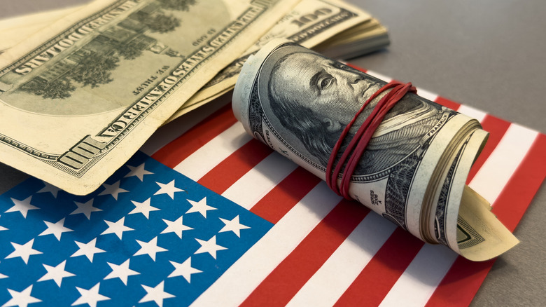 A stack and a wad of $100 bills laying on top of an American Flag