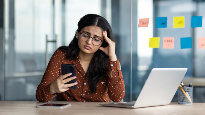 Sad woman looks at her smartphone in her office