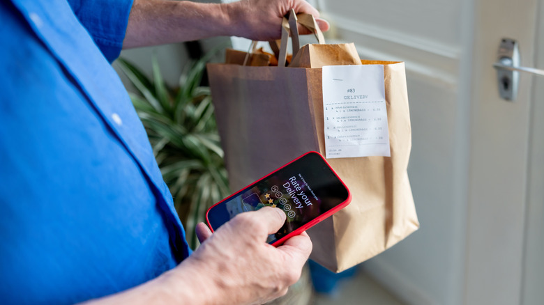 Man in blue shirt holding food delivery and rating it on app