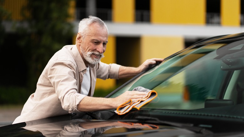 Senior man wiping down car with cloth