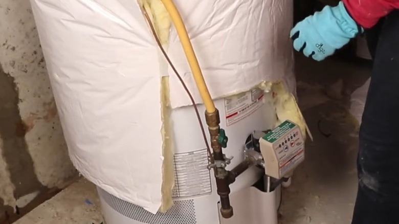 Person wrapping a water heater in an insulation blanket