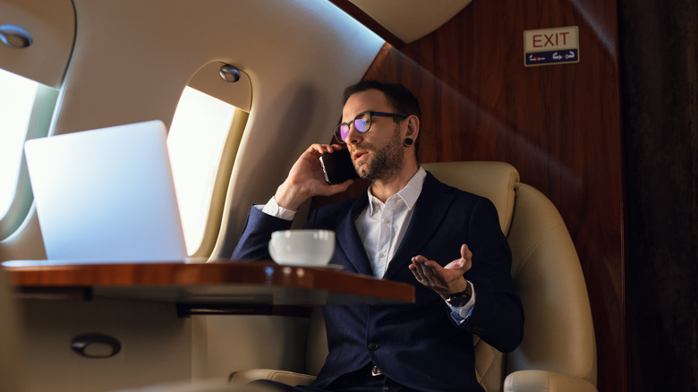 A wealthy businessman talking on a phone on a private jet.