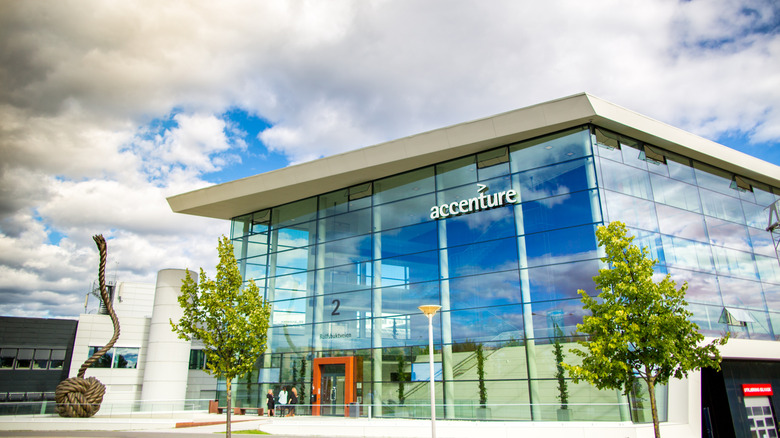 The exterior of a building with high glass walls and an Accenture logo on a cloudy day