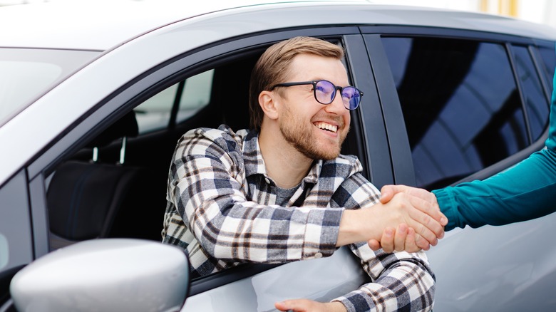 Man shaking hands while leaning out of car window